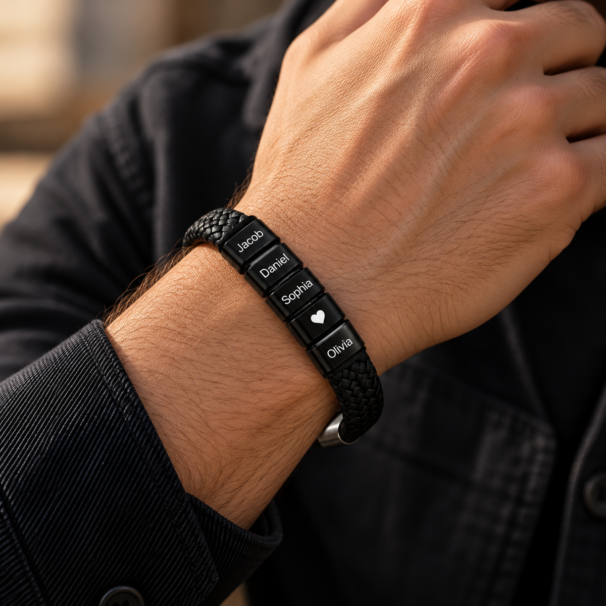 Close-up of a men's personalized black braided leather bracelet worn on the wrist, featuring custom engraved family names and a heart charm. A meaningful Father's Day gift for Dad or husband.