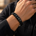 Close-up of a men's personalized black braided leather bracelet worn on the wrist, featuring custom engraved family names and a heart charm. A meaningful Father's Day gift for Dad or husband.