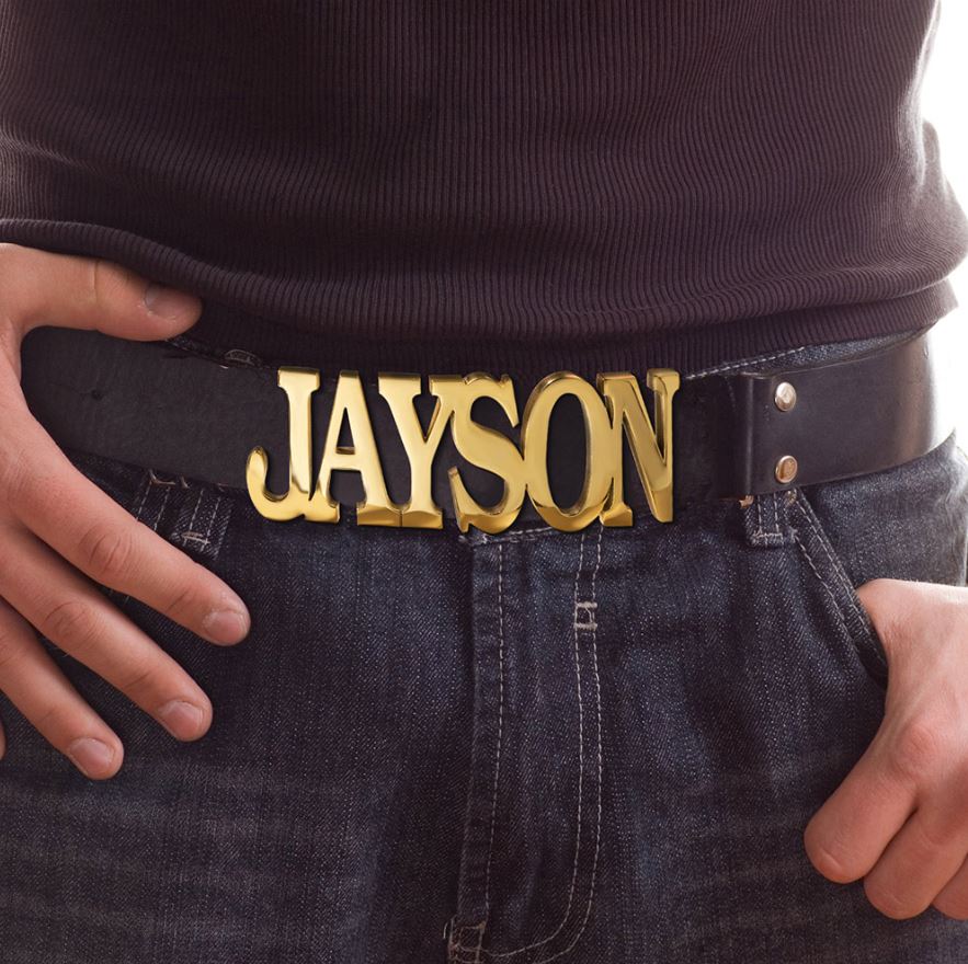 Close-up of a person wearing a dark belt with a custom gold buckle spelling 'JAYSON' over denim jeans.