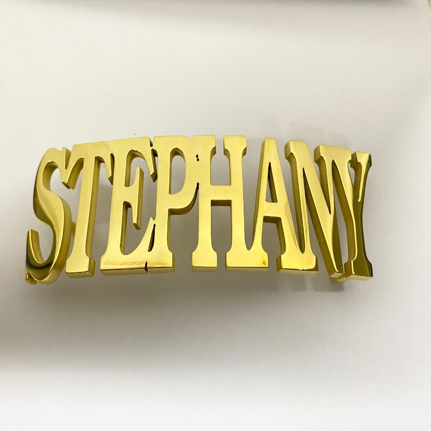 Gold belt buckle with the name 'STEPHANY' in bold, cut-out letters, displayed on a white surface.