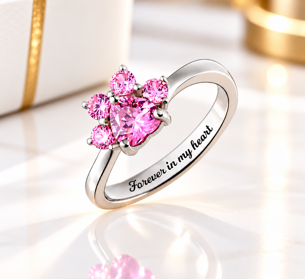 Pink cubic zirconia paw print birthstone ring in 925 sterling silver with Forever in my heart engraving, displayed on black leather.