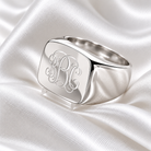 Personalised sterling silver square signet ring with engraved monogram initials on elegant white satin.