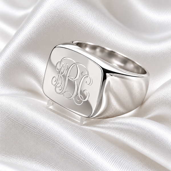 Personalised sterling silver square signet ring with engraved monogram initials on elegant white satin.