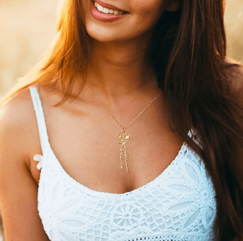 Woman wearing a gold Personalized Birth Flower Necklace with custom names, displayed against a white crocheted top, featuring a delicate and elegant design.