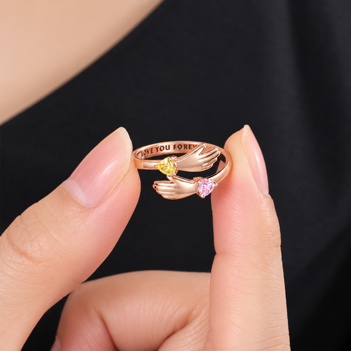A close-up of a person's fingers holding a rose gold hug ring with birthstone