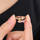 A close-up of a person's fingers holding a rose gold hug ring with birthstone