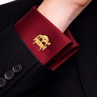 Gold interlocking initials cufflink worn on a burgundy formal shirt cuff with a black suit