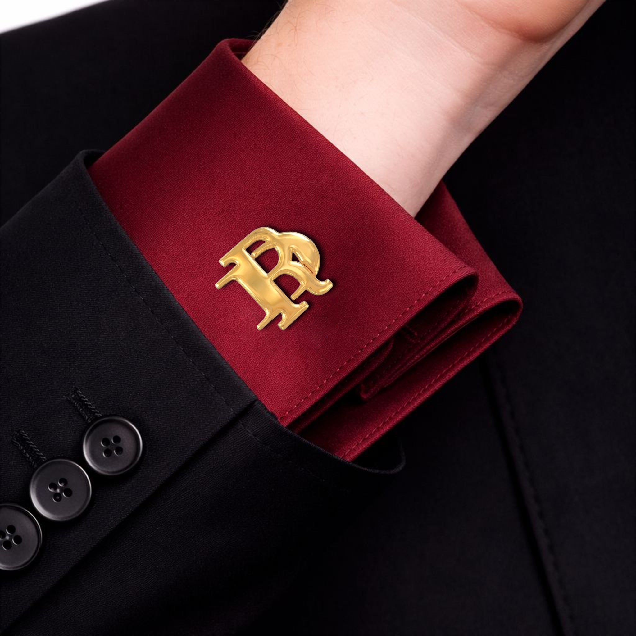 Gold interlocking initials cufflink worn on a burgundy formal shirt cuff with a black suit