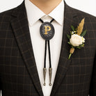 Custom bolo tie with gold letter P, worn with plaid suit and white rose boutonniere for formal occasions.