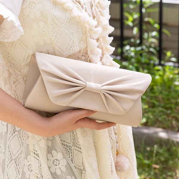 Elegant cream clutch with bow detail, held by woman in lace dress for special occasions