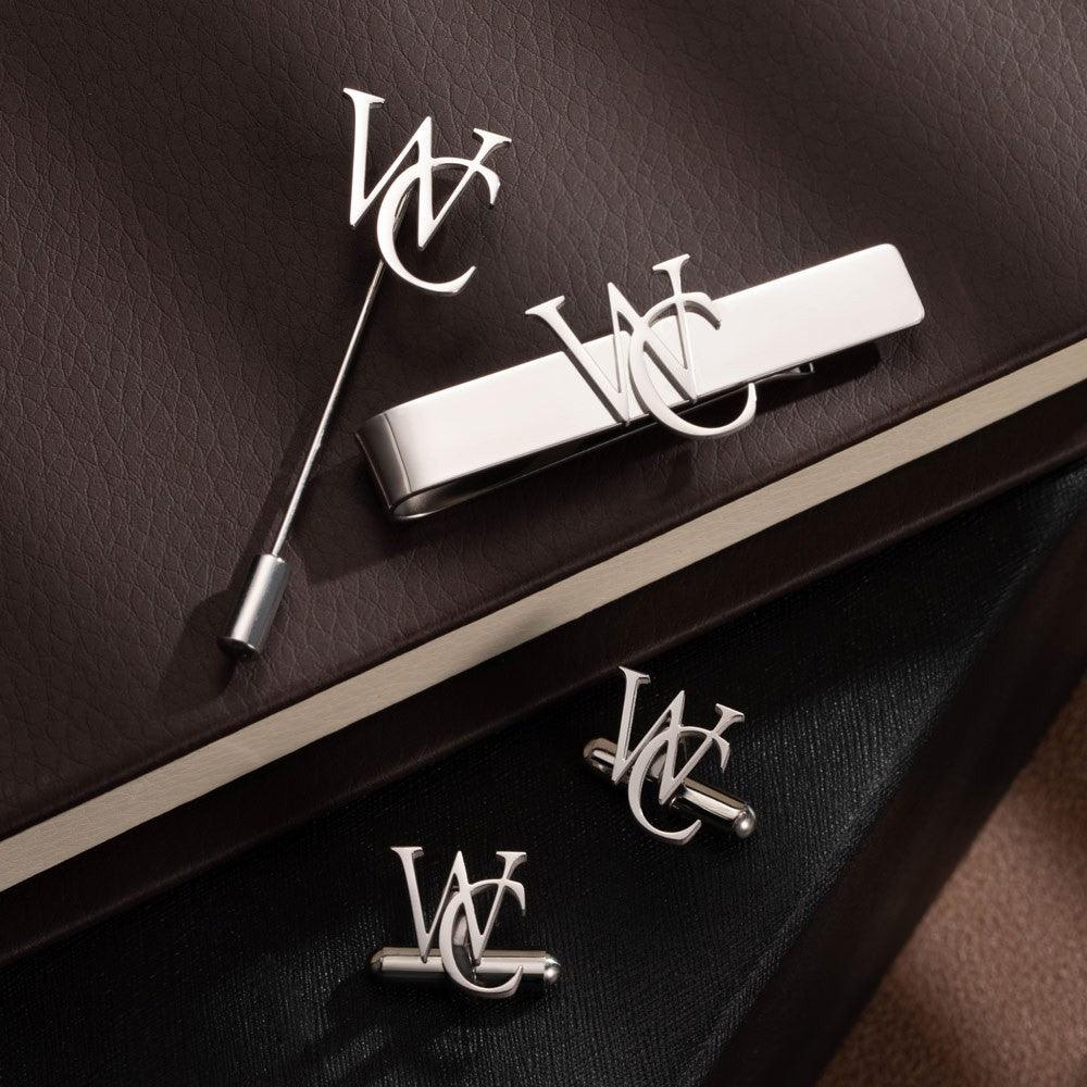 Personalized monogrammed cufflinks, lapel pin, and tie bar displayed on leather surface.