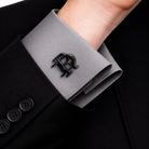 Black interlocking initials cufflink worn on a grey formal shirt cuff with a black suit.