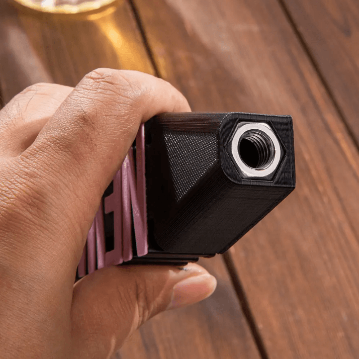 A close-up of a person's hand holding a black 3D printed beer tap handle with a metallic threaded insert, on a wooden table with a beer glass in the background.