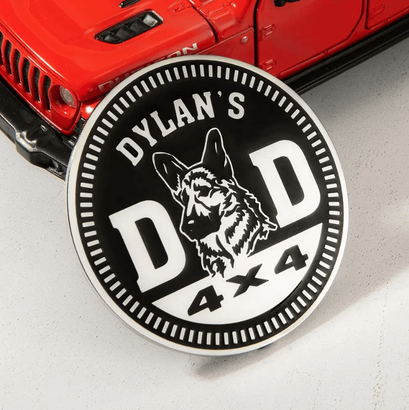 Close-up of a custom 'Dylan's Dad 4x4' badge with a German Shepherd design on a red Jeep hood.