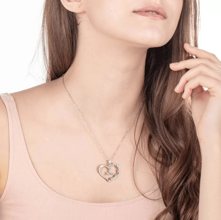 A young woman wearing a silver heart-shaped necklace with "Nana" inscribed and adorned with colorful gemstones and names around the edge.