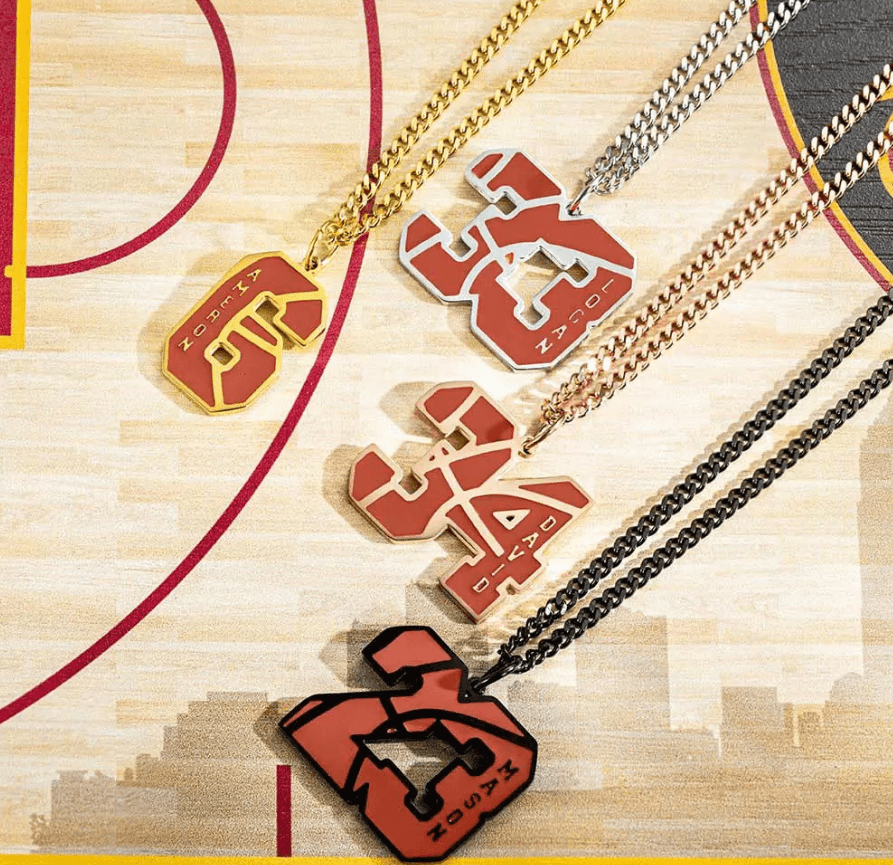 Four basketball-themed pendants in different metals featuring various numbers and names, laid out on a basketball court design.