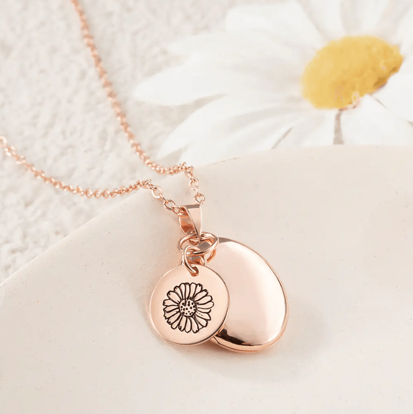 Rose Gold Personalized Birth Flower Necklace with Oval Photo Locket, featuring a flower engraving, displayed on a light surface with a white daisy in the background.