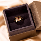 A gold college ring with a red gemstone, inscribed with "COLLEGE LOS ANGELES," "2024," and "GRACE" with an Om symbol, displayed in an open black velvet box.