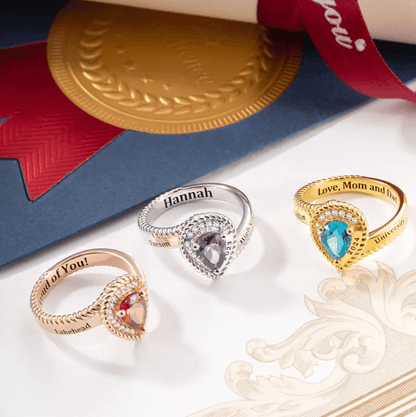 Assorted personalized class rings in gold and silver with engraved names and messages, displayed with diploma and ribbon.