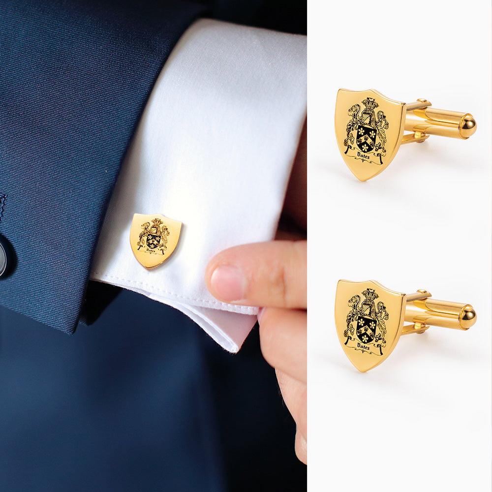 Gold shield-shaped cufflinks with intricate family crest design, worn on a white shirt cuff.