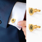 Gold shield-shaped cufflinks with intricate family crest design, worn on a white shirt cuff.