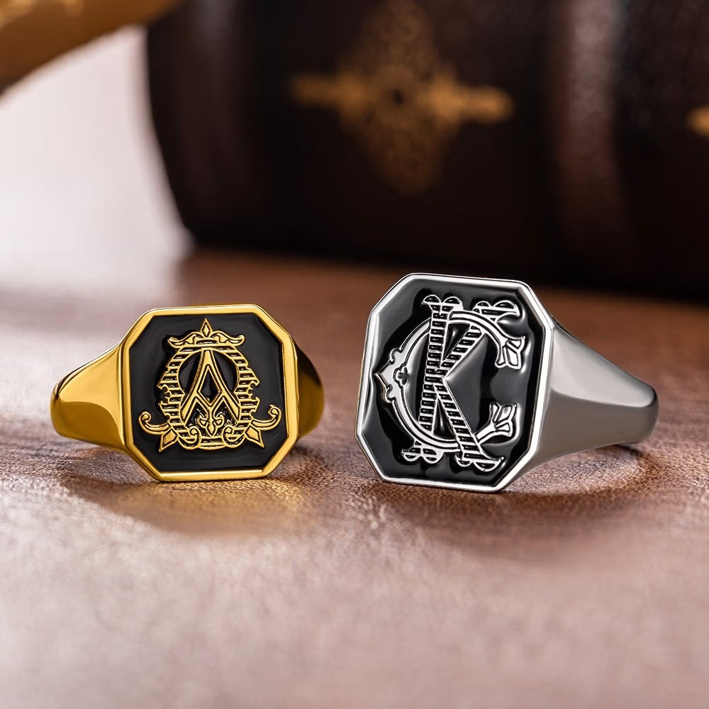 Gold and silver tone engraved initials signet rings with black faces in square and octagonal styles.