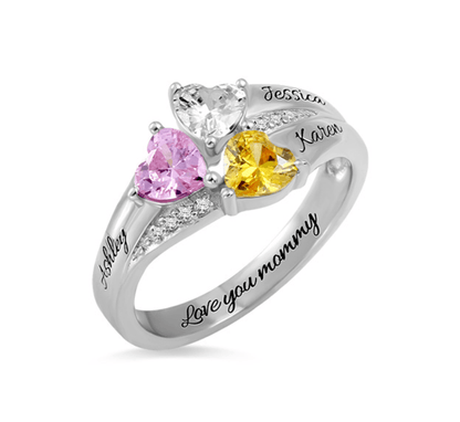 A silver ring with three heart-shaped gemstones in clear, pink, and yellow, personalized with the names Jessica, Karen, Ashley, and the inscription "Love you mommy."