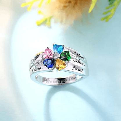 A silver ring with five heart-shaped gemstones in pink, blue, green, yellow, and blue, personalized with the names Cara, Olivia, Aaron, Eileen, and Hunt, on a light background.