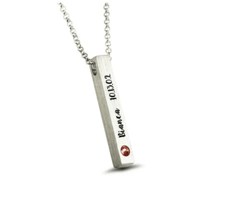 A silver necklace with a vertical bar pendant engraved with "Bianca 10.13.02" and a red gemstone on the bottom left corner, displayed on a white background.