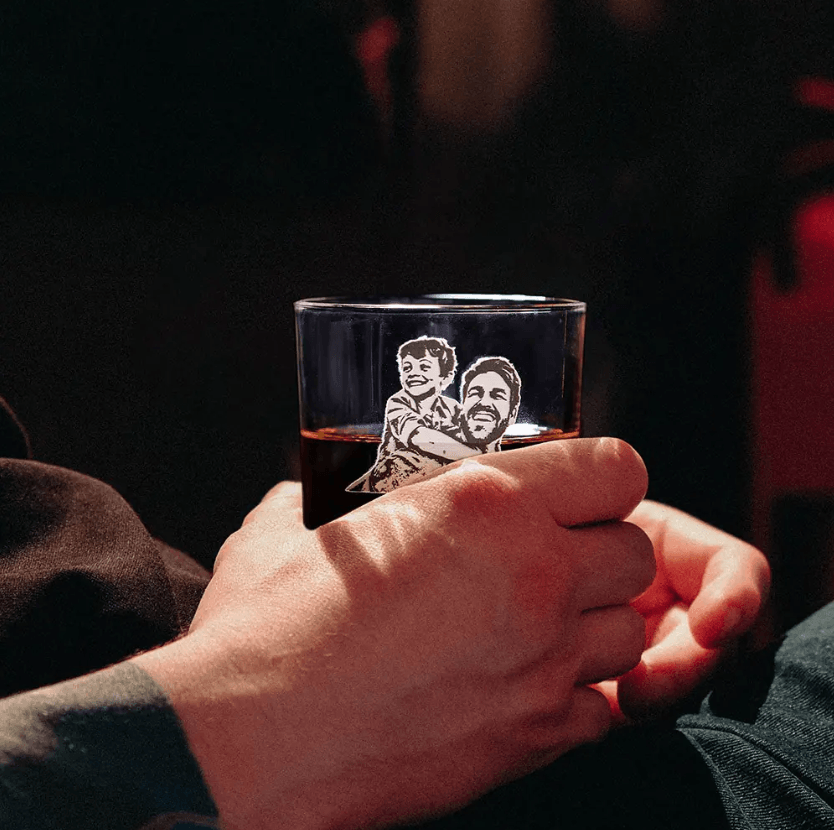 Hand holding a custom engraved whiskey glass with a family photo of a father and child, labeled "Dad & Daniel.