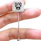 Close-up image of a personalized family crest lapel pin held between two fingers, showcasing intricate design and the name 'Robitaille' engraved on it.