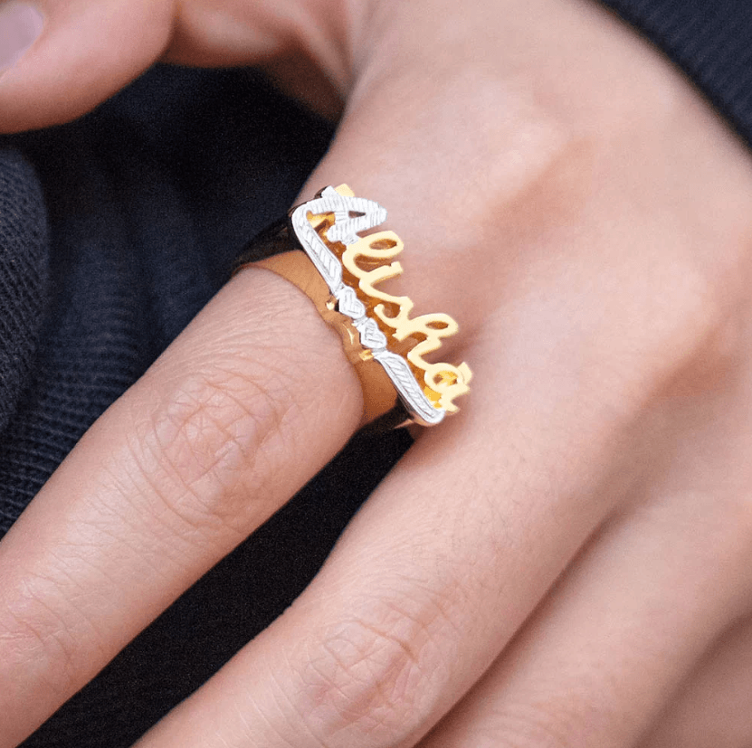 Gold and silver personalized name ring with 'Alisha' in large script on a woman's finger.