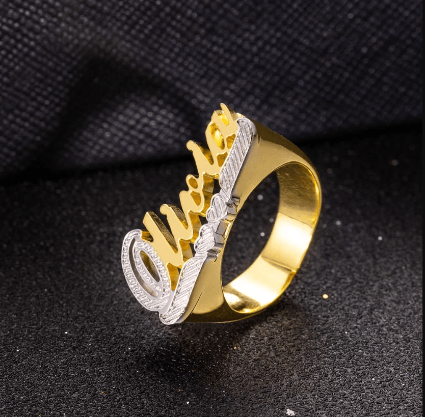 Elegant gold 'Olivia' name ring with silver details, standing upright on a dark textured background.