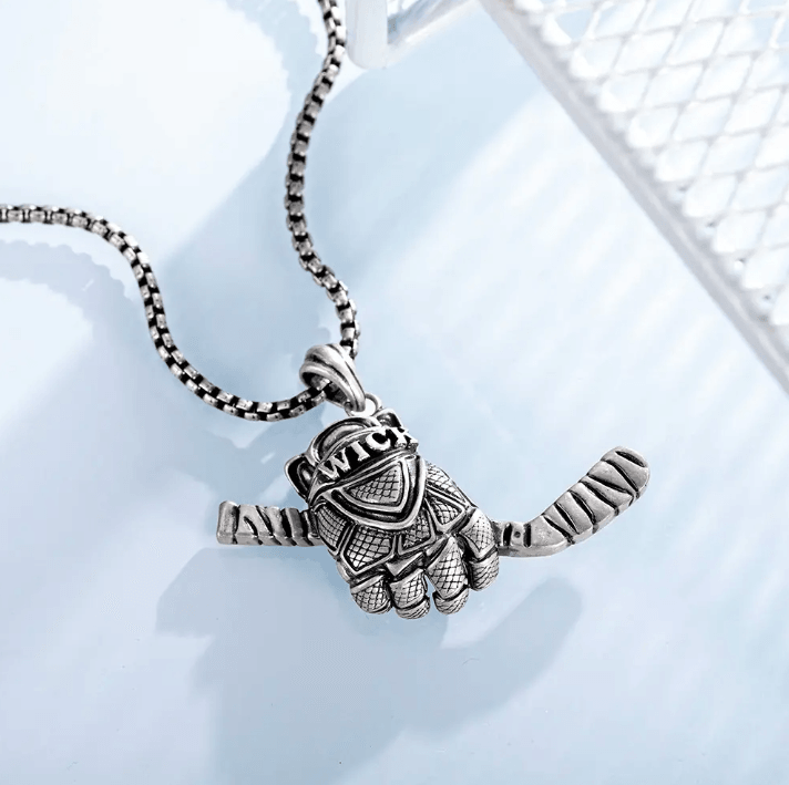 A silver necklace with a pendant shaped like a detailed hockey glove holding a single hockey stick, displayed on a light blue background.