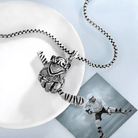 A silver necklace with a pendant shaped like a detailed hockey glove holding a single hockey stick, displayed on a white plate with a photo of a hockey player.