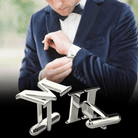 Man adjusting cufflinks on a navy suit, with close-up of silver initial cufflinks displaying letters 'MH'.