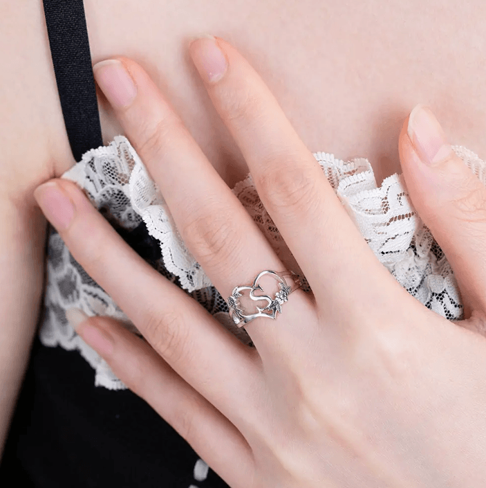 Silver heart-shaped ring with intricate flower detailing on a woman's finger, highlighting elegant lace fabric background.