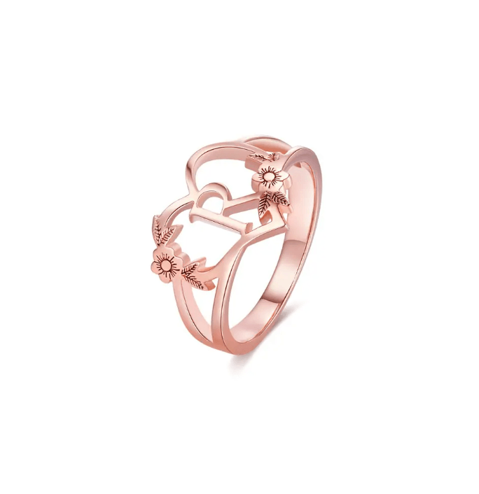 Rose gold ring with intertwined initial 'A' and floral detailing on a clean white backdrop.