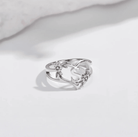 "Silver monogram ring with the initial 'S' entwined in a heart shape with floral detail, against a soft white shadowed background.