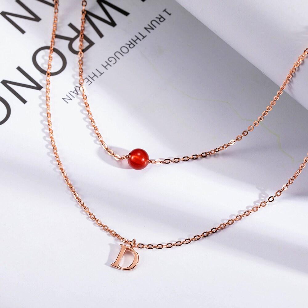 Custom Layered Initials and Tiny Moonstone Birthstone Necklace in rose gold with a 'D' initial charm and a red moonstone bead on delicate chains.