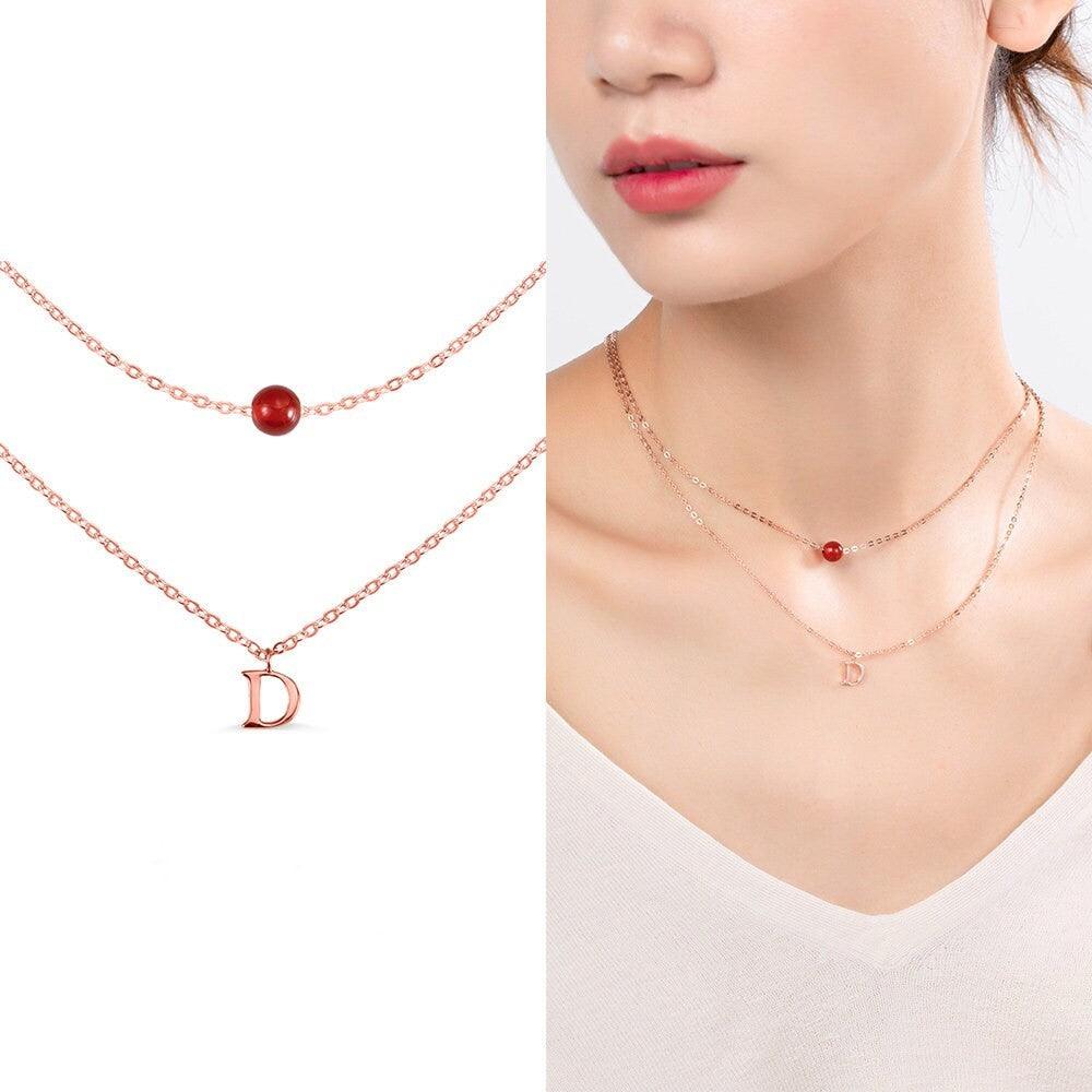 Custom Layered Initials and Tiny Moonstone Birthstone Necklace in rose gold with a 'D' initial charm and red moonstone bead, worn by a woman.