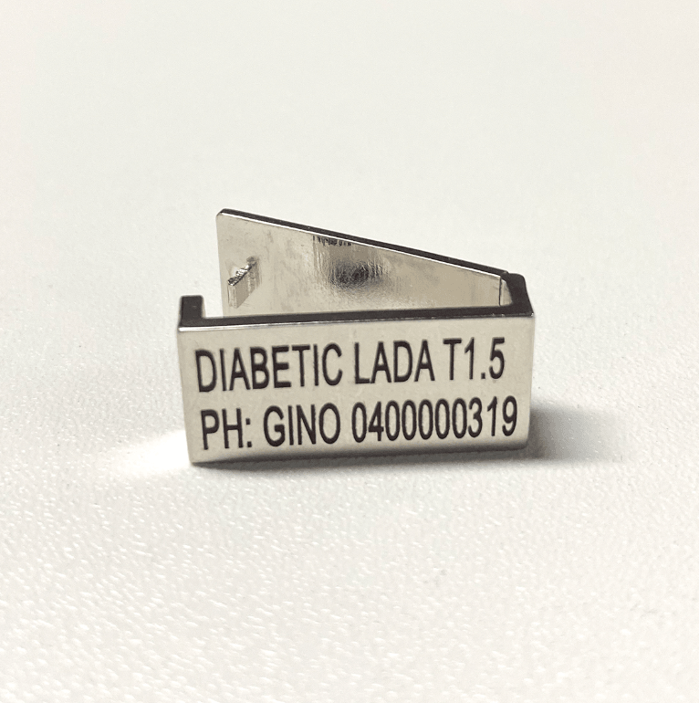 A silver medical tag with the inscription "DIABETIC LADA T1.5 PH: GINO 0400000319" displayed on a white background.