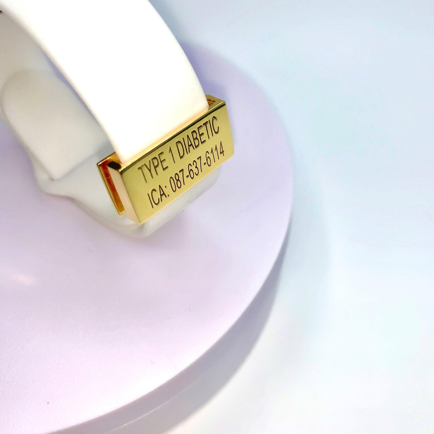 A gold medical tag attached to a white band with the inscription "TYPE 1 DIABETIC ICA: 087-637-6114" displayed on a white background.