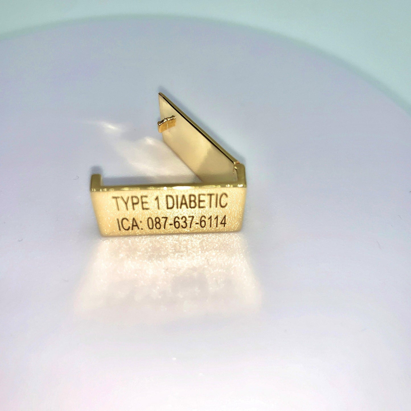 A gold medical tag with the inscription "TYPE 1 DIABETIC ICA: 087-637-6114" displayed on a white background.