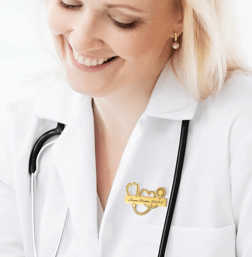 Smiling healthcare professional wearing a Personalized Medical School Graduation Lapel Pin with a custom stethoscope design on a white lab coat.