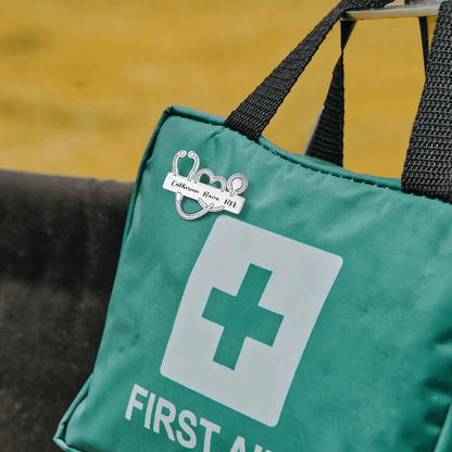 Personalized Medical School Graduation Lapel Pin with custom stethoscope design attached to a green first aid kit bag with "First Aid" text.