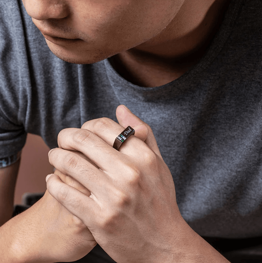 Close-up of a man wearing a black 'Dad' engraved ring with multicolored birthstones.