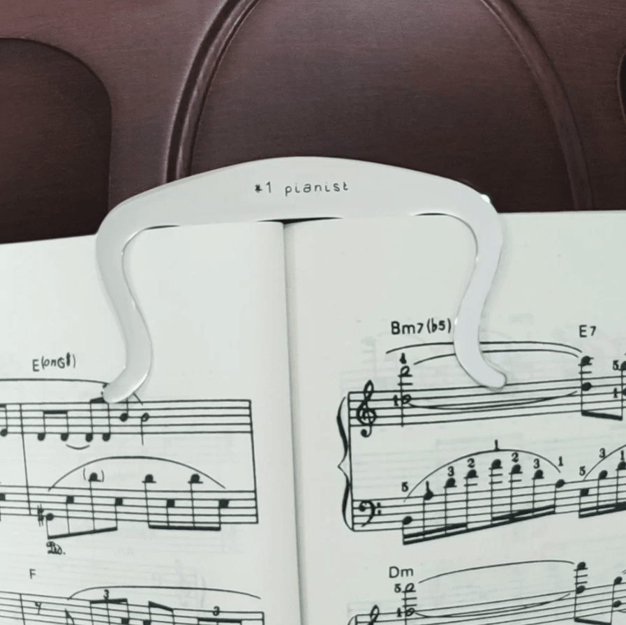 White music book holder clip labeled '#1 pianist' on open sheet music, with a guitar in the back.