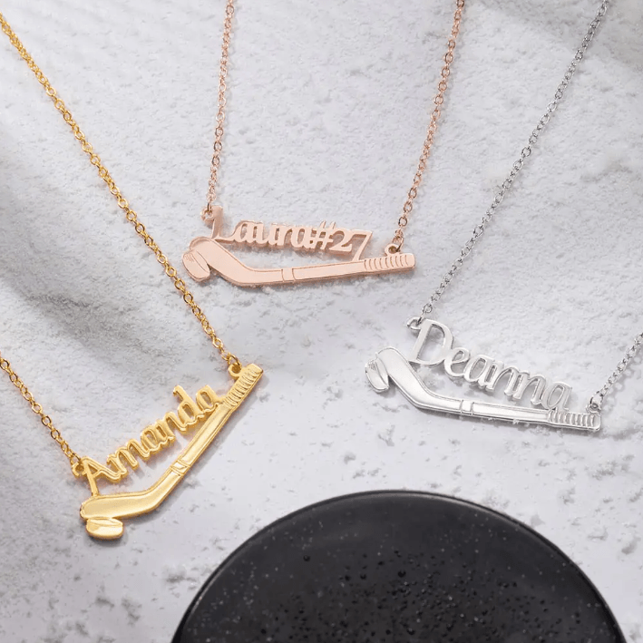 Three necklaces with names "Amanda," "Laura#27," and "Deanna" featuring a hockey stick and puck design in gold, rose gold, and silver finishes respectively.