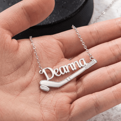A hand holding a silver necklace with the name "Deanna" elegantly scripted, featuring a hockey stick and puck design.